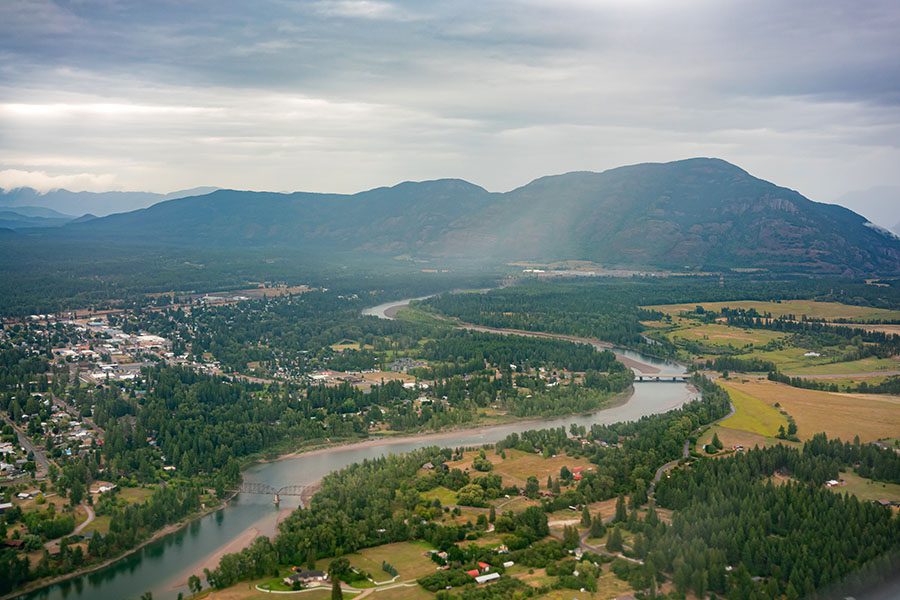 Kalispell MT - Aerial View of the City of Kalispell in Montana Surrounded by Green Foliage and Mountains