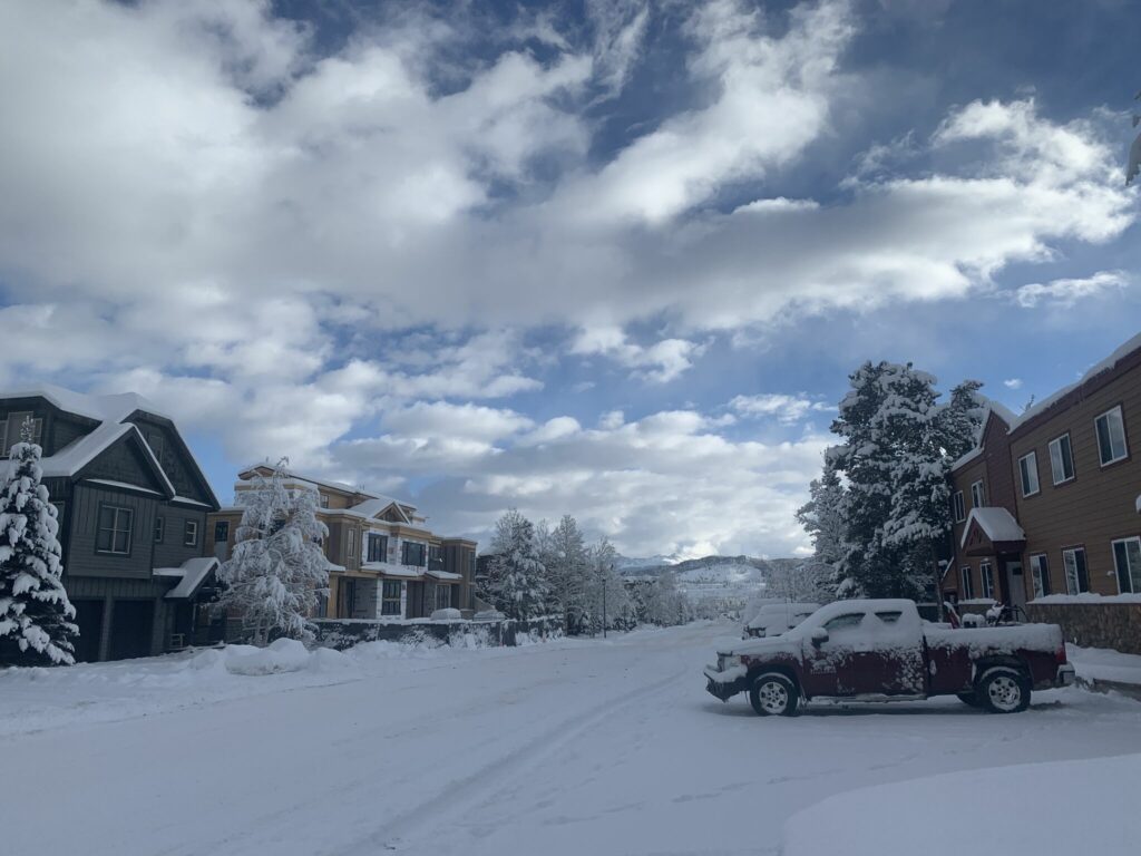 snowy road of homes under blue skies with clouds
