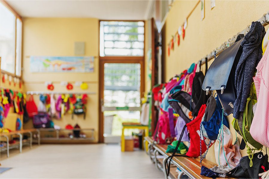 Daycare Insurance Coverage - Daycare Room with Colorful Kids Jackets, Hats, Boots, and Other Items Handing on the Walls and the Open Door to the Daycare is Blurred in the Background